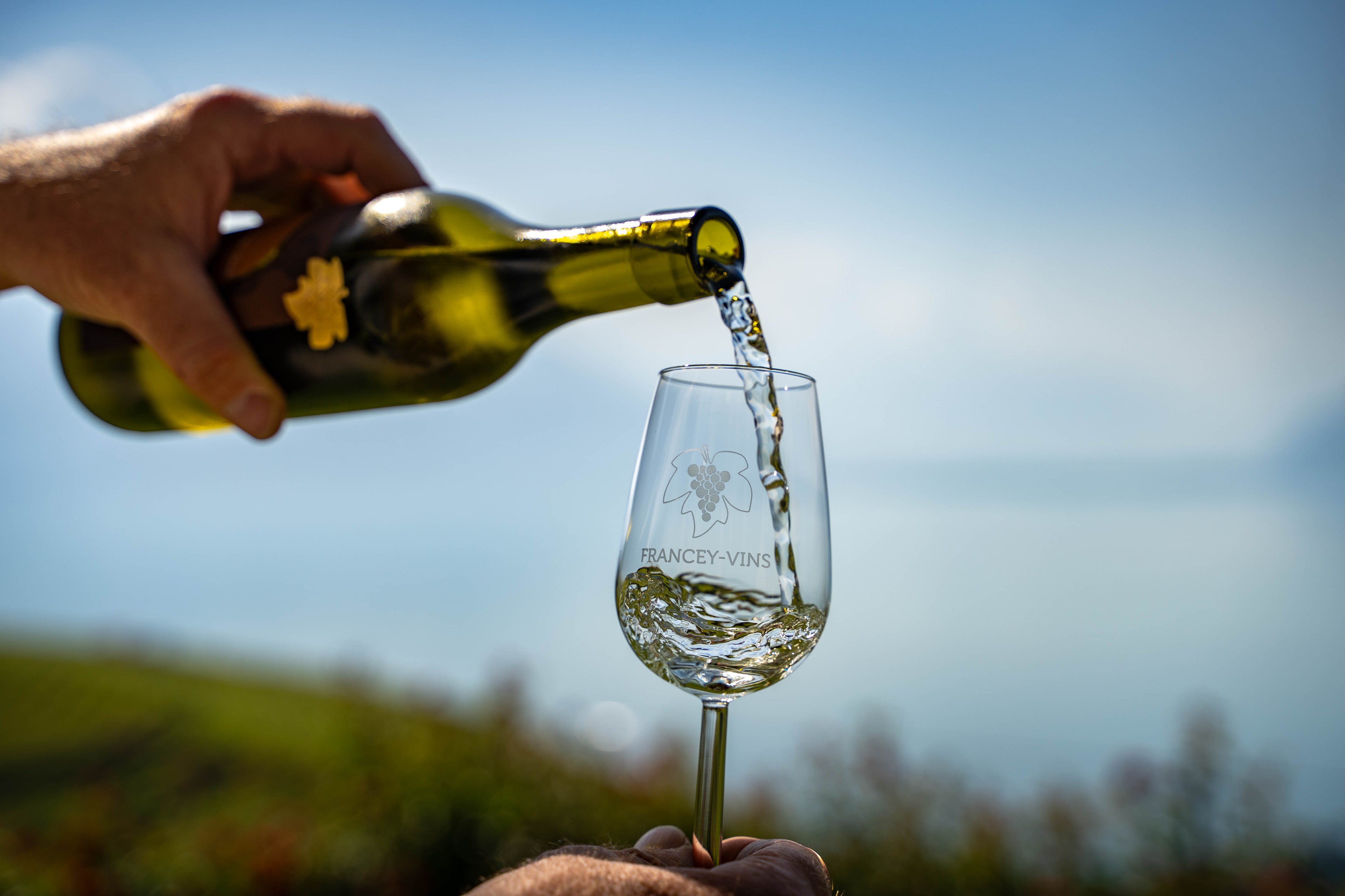 Vin Francey Vins servi dans un verre de dégustation, avec vue sur le lac Léman et les vignobles de Lavaux.