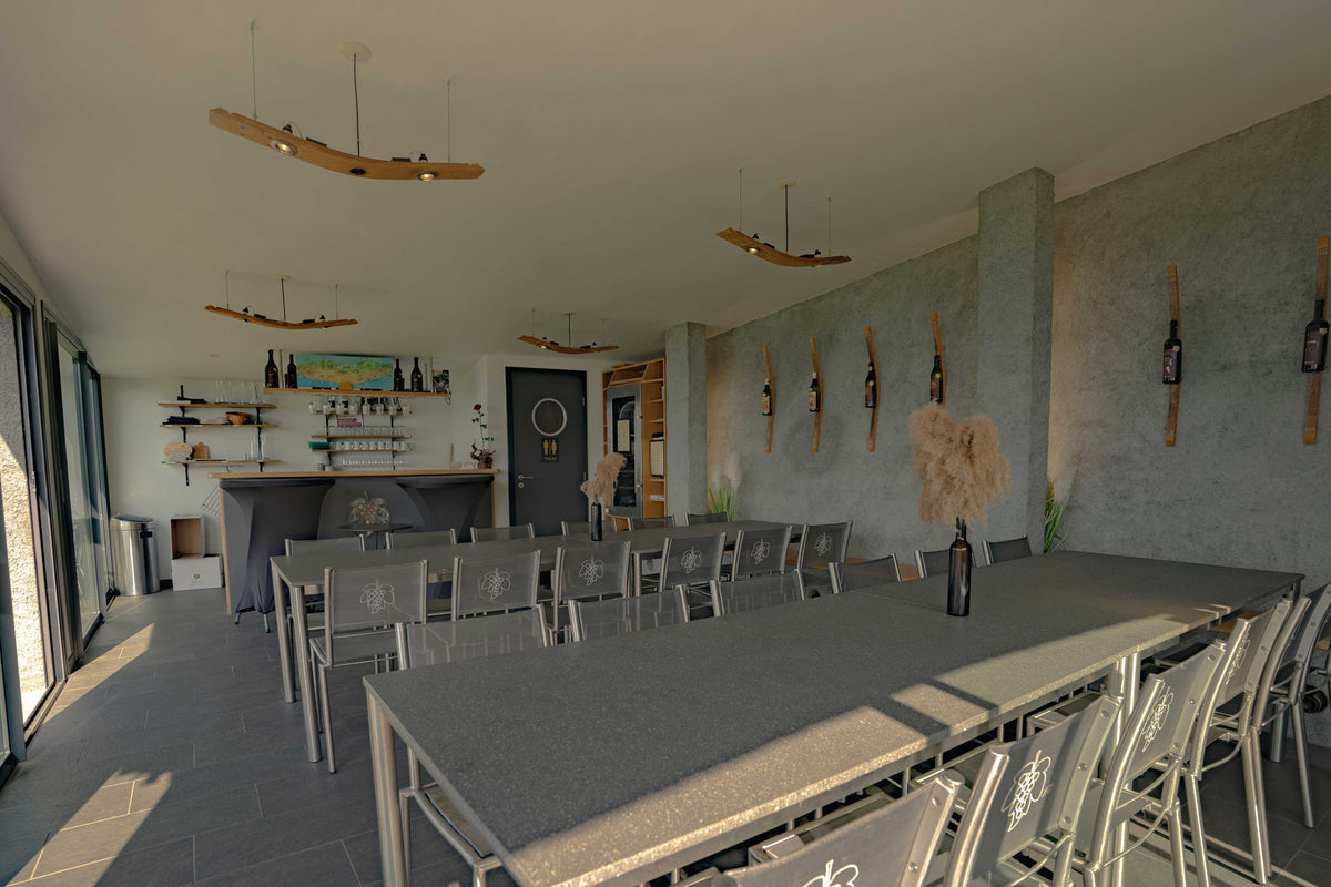 Salle événementielle La Véranda Francey Vins avec grandes tables, bar, chaises et bouteilles exposées au mur.