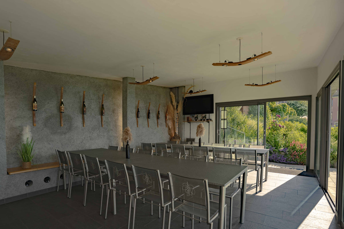 Salle événementielle La Véranda Francey Vins avec tables, chaises, bouteilles exposées au mur et accès direct au jardin.
