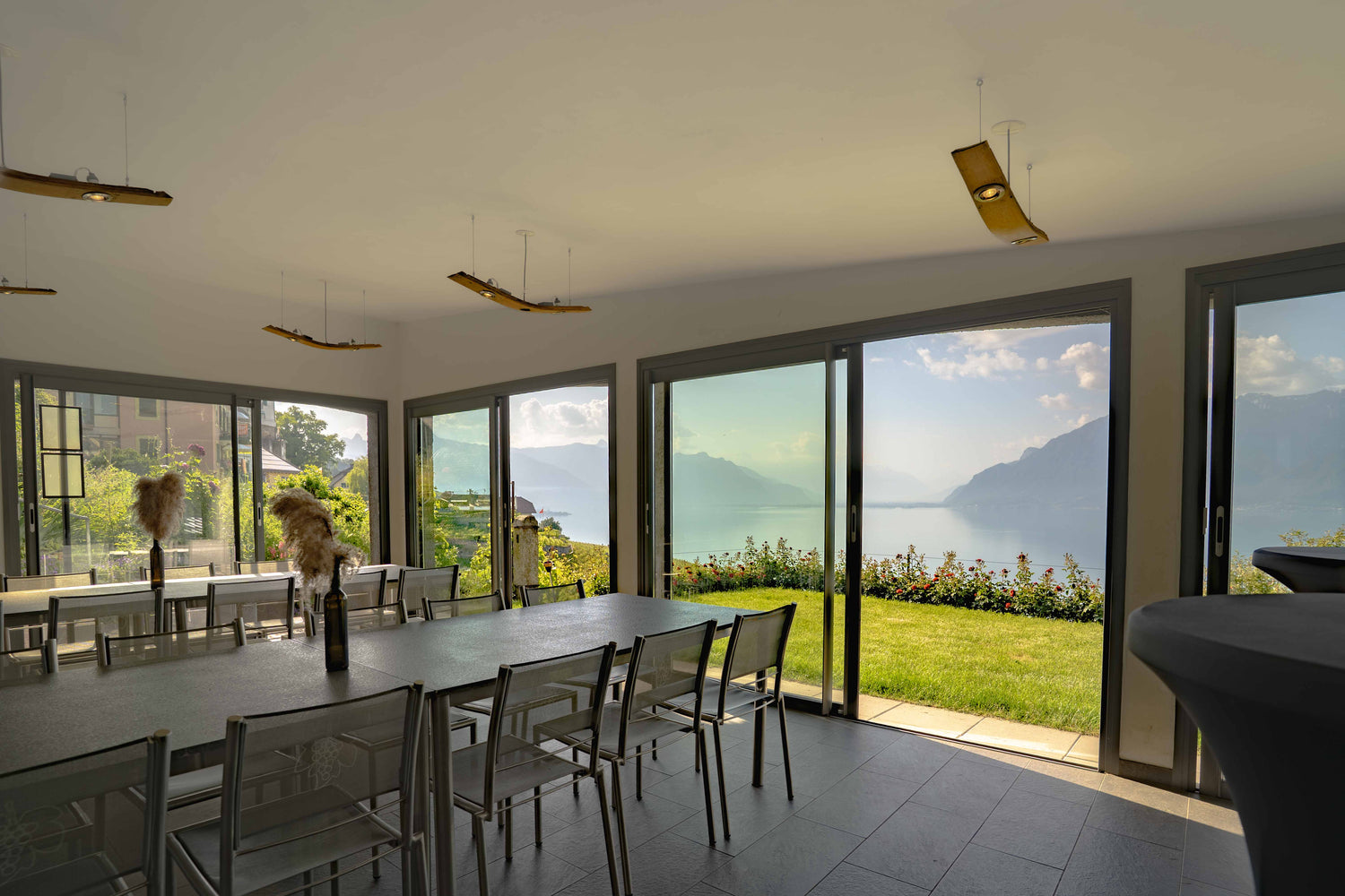La Véranda Francey Vins avec grandes tables, baies vitrées et vue panoramique sur le jardin, le lac Léman et les montagnes.
