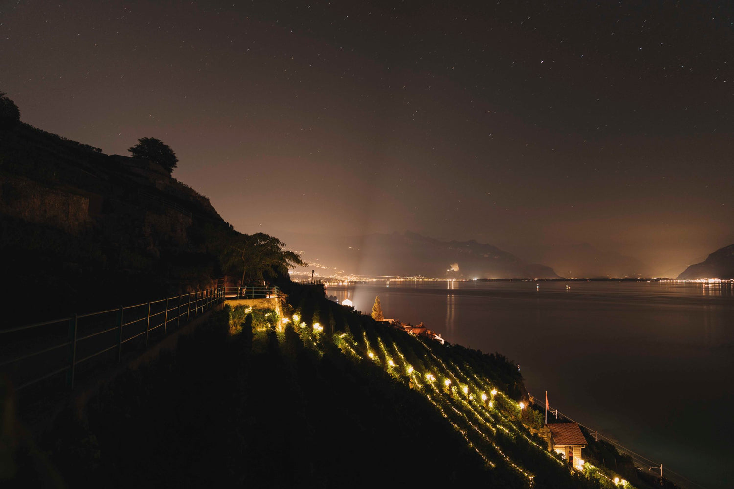 Vue nocturne sur les vignobles illuminés de Lavaux, le lac Léman et les lumières au loin.